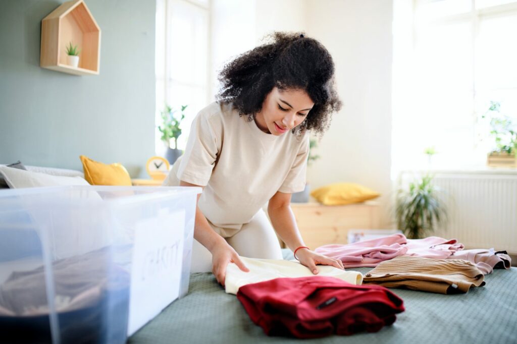 A young woman folds sweaters and packs them in a storage bin