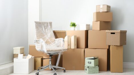 A stack of moving boxes and a plastic-wrapped desk chair sit against a wall