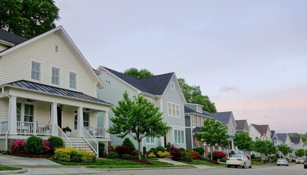 A row of houses along the road with a couple cars parked in the street