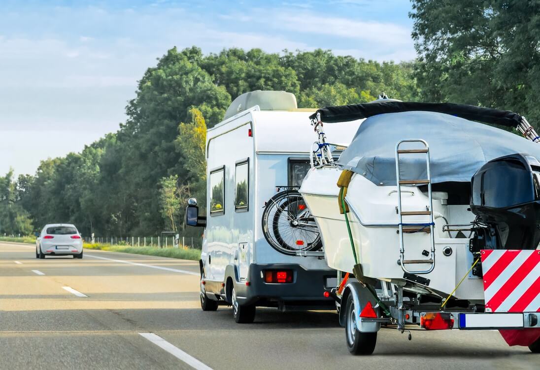 RV driving on the highway towing a boat behind.