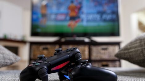 Two console controllers in front of a soccer game on the television.