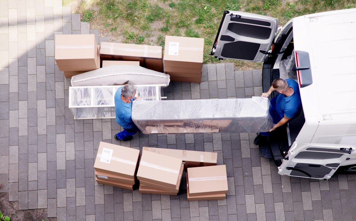 Two movers carry a large piece of furniture into a moving van.