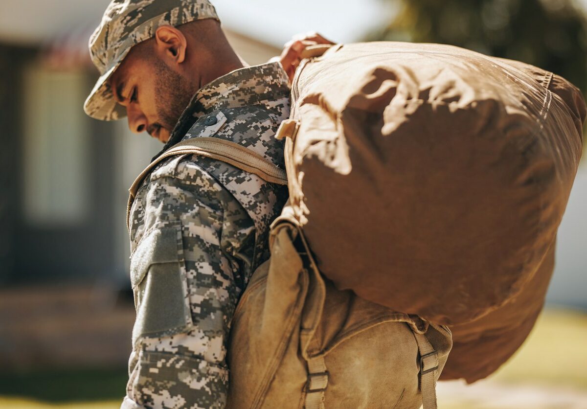 A service member returning home with his gear over his shoulder.