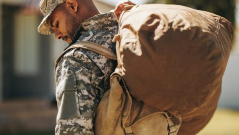 A service member returning home with his gear over his shoulder.