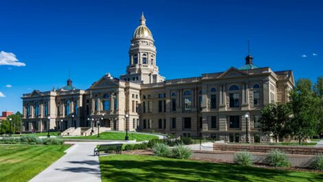 The Wyoming State Capitol, a large historic building with a gold dome, surrounded by a manicured lawn and blue skies.