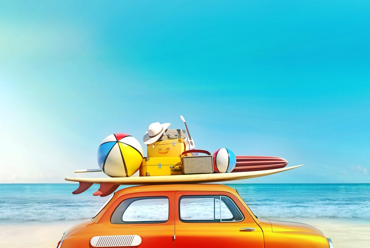 A small orange car with a surfboard and beach gear stacked on the roof next to the ocean.